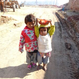 Two children stand at brick kiln, one with a basket of clay on her head