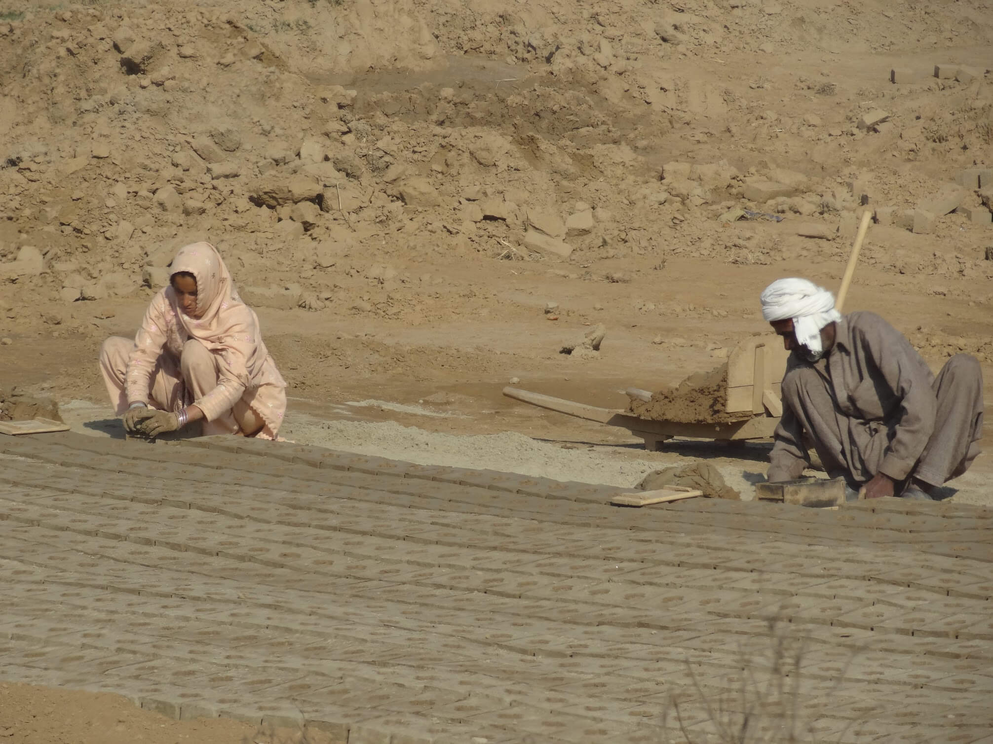 Two laborers make bricks behind rows and rows of drying bricks.