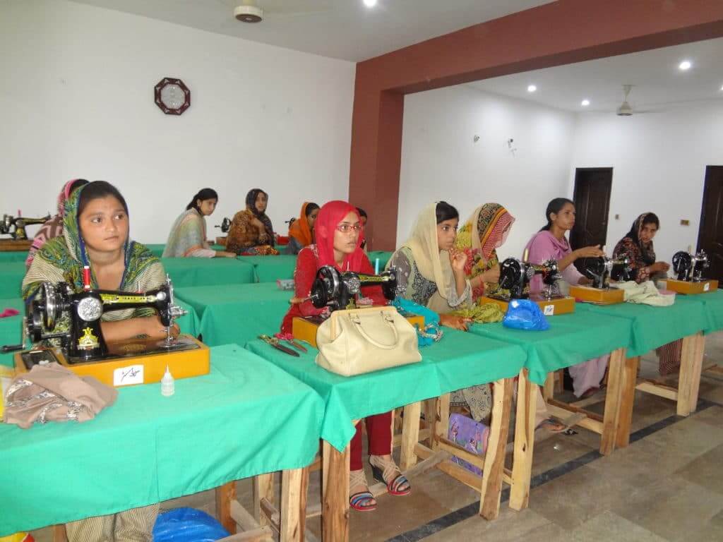 RAM Foundation Empowering Women in Pakistan Women sit at sewing machines on individual tables with green table cloths.