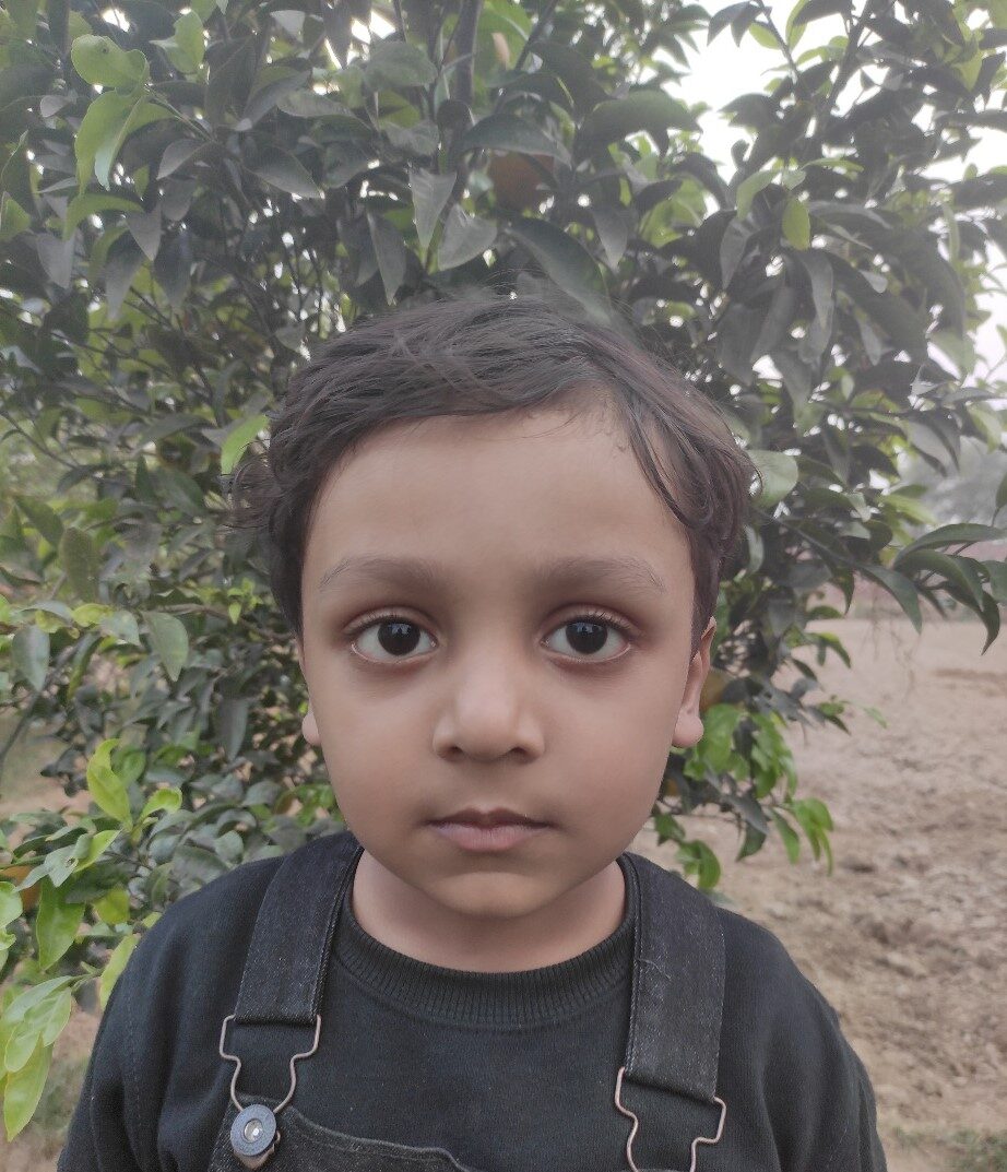 Lian A young Pakistani boy in black clothes stands in front of a tree.