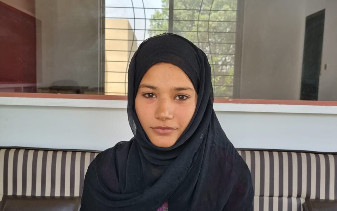 A young woman wearing a black headscarf sits on a sofa.